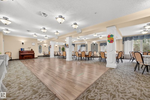 Expansive common area featuring wood-finish flooring, patterned carpeting, multiple decorative columns, and numerous ceiling-mounted light fixtures - #420 9820 165 St Nw, Edmonton, AB 