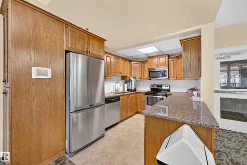 Wood-finish cabinetry, stainless steel appliances, granite-style countertops, tile flooring, and a white subway tile backsplash - #420 9820 165 St Nw, Edmonton, AB 