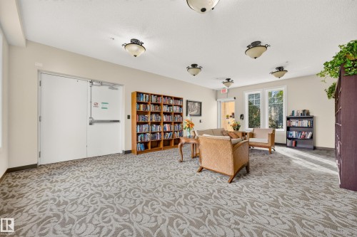 Spacious common area featuring patterned carpeting, multiple flush-mount ceiling lights, and built-in shelving - #420 9820 165 St Nw, Edmonton, AB 