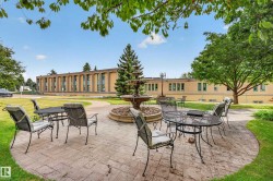 Expansive outdoor entertaining patio featuring circular stone hardscaping with a central fire pit, surrounded by mature landscaping and lush lawn - 