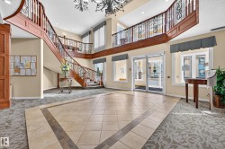 Two-story foyer featuring a grand staircase with wood-finish railings and wrought iron detailing, large format tile flooring with a decorative border, patterned carpet, and tall windows - 