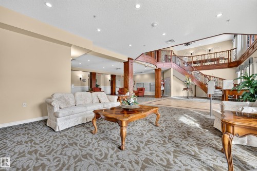 Spacious lobby featuring a grand double staircase with ornate railings, recessed lighting, and patterned carpeting - #420 9820 165 St Nw, Edmonton, AB 