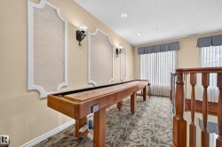 Carpeted room with decorative wall panels, wall sconces, window treatments, and wood railings - 