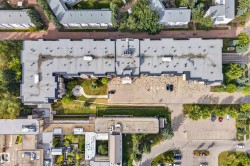 Aerial perspective highlighting a large building with a flat roof, an interior courtyard featuring a circular landscaped area, adjacent parking areas, and surrounding mature trees - 