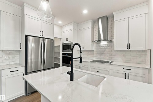 White shaker-style cabinetry, stainless steel appliances, a center island with an integrated sink, a tiled backsplash, and recessed lighting - 5852 Raven Crescent Nw, Edmonton, AB 
