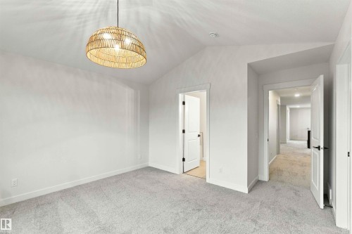 Vaulted ceiling featuring a woven pendant light fixture, soft gray carpeting, and white interior doors with dark hardware - 5852 Raven Crescent Nw, Edmonton, AB 