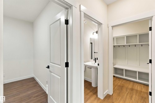 Hallway featuring wood-finish flooring, a built-in mudroom bench with shelving and coat hooks, a pedestal sink, and a framed mirror - 5852 Raven Crescent Nw, Edmonton, AB 
