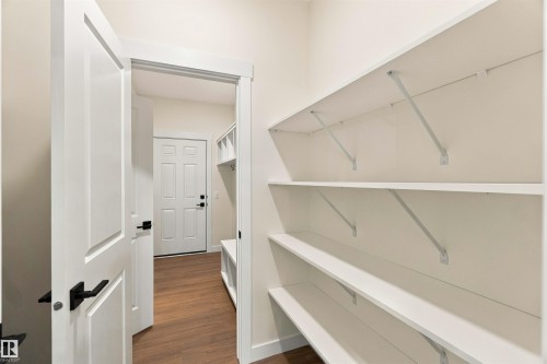 Built-in shelving for storage, paneled interior door with matte black hardware, wood-finish flooring, and white trim throughout - 5852 Raven Crescent Nw, Edmonton, AB 