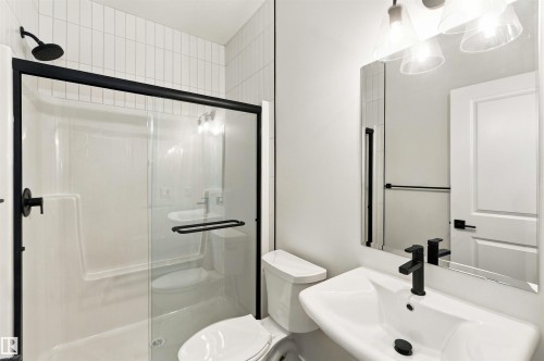 Shower with black-framed glass enclosure, white subway tile surround, wall-mounted vanity with integrated sink, black single-handle faucet, and rectangular mirror - 5852 Raven Crescent Nw, Edmonton, AB 
