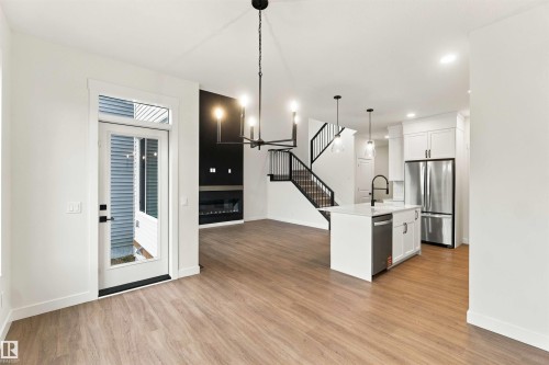 Open-concept living space with wood-finish flooring, a contemporary fireplace, a kitchen island with stone countertops, stainless steel appliances, and a modern chandelier - 5852 Raven Crescent Nw, Edmonton, AB 