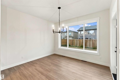 Spacious room featuring wood-finish flooring, ample natural light from a large window, a contemporary chandelier, and a white interior door - 5852 Raven Crescent Nw, Edmonton, AB 