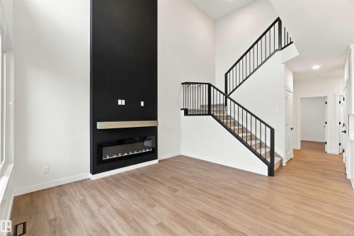 Two-story living space featuring a modern fireplace with a wood mantel, wood-finish flooring, and an open staircase with black metal railings - 5852 Raven Crescent Nw, Edmonton, AB 