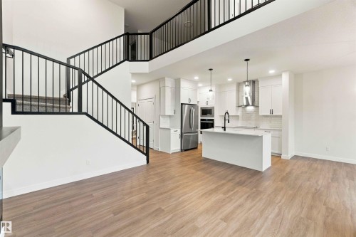 Two-story ceiling, open-concept kitchen with white cabinetry, large kitchen island with pendant lighting, stainless steel appliances, and wood-finish flooring - 5852 Raven Crescent Nw, Edmonton, AB 