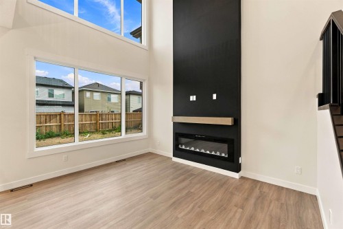 Expansive windows with high ceilings, wood-finish flooring, linear electric fireplace, and a light wood-tone mantel - 5852 Raven Crescent Nw, Edmonton, AB 