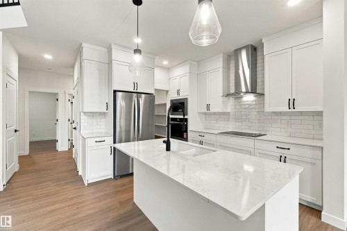 White cabinetry with black hardware, stainless steel appliances, wood-finish flooring, white subway tile backsplash, and a large central island with an integrated sink - 5852 Raven Crescent Nw, Edmonton, AB 