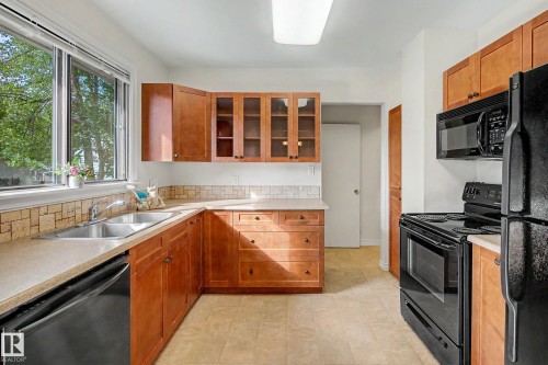 Kitchen featuring wood cabinetry, a double basin stainless steel sink, black appliances, and a tiled backsplash - 10830 138 Street Nw, Edmonton, AB 