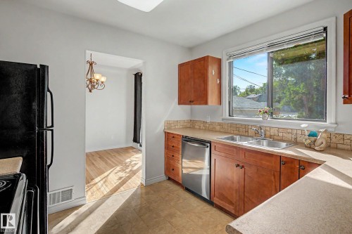 Kitchen featuring wood cabinetry, a double basin stainless steel sink, stainless steel dishwasher, and tile backsplash - 10830 138 Street Nw, Edmonton, AB 