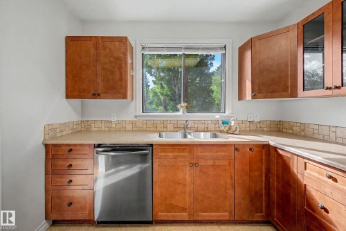 Wood-finish cabinetry with dark hardware, a double basin stainless steel sink, and a stainless steel dishwasher - 10830 138 Street Nw, Edmonton, AB 