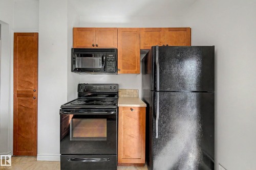 Kitchen featuring wood-finish cabinetry, black appliances, a built-in microwave, and a tile backsplash - 10830 138 Street Nw, Edmonton, AB 