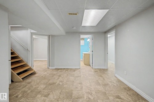 Spacious room with neutral wall tones, patterned flooring, wood staircase, and recessed ceiling lighting - 10830 138 Street Nw, Edmonton, AB 