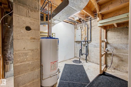 Basement utility area featuring a water heater, exposed ductwork, and visible concrete block foundation walls - 10830 138 Street Nw, Edmonton, AB 