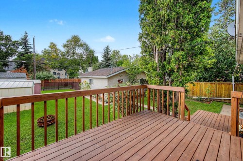 Expansive wood-finish deck with railings, offering access to a manicured lawn and mature perimeter trees - 10830 138 Street Nw, Edmonton, AB 