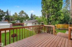 Expansive wood-finish deck with railings, offering access to a manicured lawn and mature perimeter trees - 