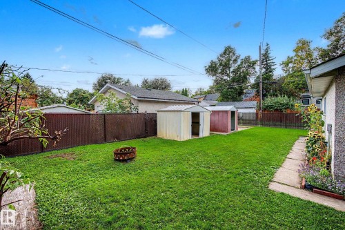 Expansive lawn area with two storage sheds, a concrete walkway, and a perimeter fence - 10830 138 Street Nw, Edmonton, AB 