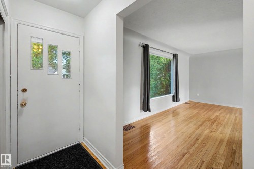 White entry door with decorative glass inserts, hardwood flooring, and a large window with privacy coverings - 10830 138 Street Nw, Edmonton, AB 