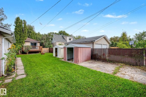 Expansive backyard featuring a detached garage, two storage sheds, a concrete patio area, and a stone-paved walkway - 10830 138 Street Nw, Edmonton, AB 