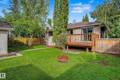 Expansive backyard featuring a wood deck, mature trees, privacy fencing, and a detached structure - 10830 138 Street Nw, Edmonton, AB 