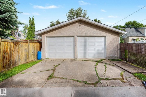 Two-car garage with stucco exterior and dual white panel doors, featuring a sloped concrete driveway - 10830 138 Street Nw, Edmonton, AB 