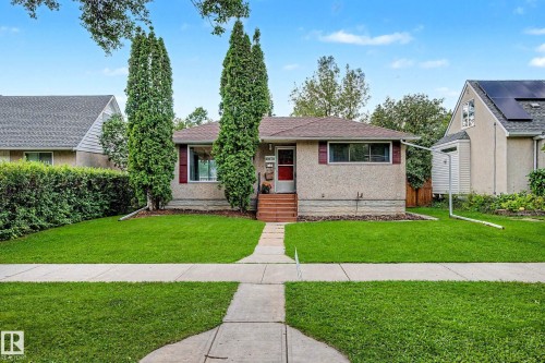 Stucco exterior with contrasting shutters, mature front yard trees, concrete walkway, and a landscaped front garden bed - 10830 138 Street Nw, Edmonton, AB 