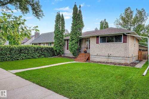 Stucco exterior with red window shutters, concrete walkway, front lawn, and mature hedges - 10830 138 Street Nw, Edmonton, AB 
