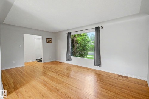 Bright interior featuring wood-finish flooring, a large picture window, and a cased opening - 10830 138 Street Nw, Edmonton, AB 