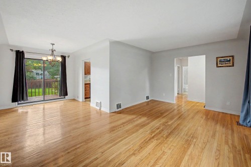 Polished wood-finish flooring throughout, bright white walls, recessed ceiling, sliding glass door to exterior, and a built-in chandelier - 10830 138 Street Nw, Edmonton, AB 