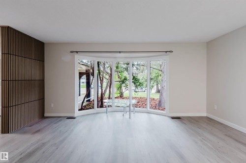 Curved bay window, light wood-finish flooring, accent wall with vertical slat detailing, white trim, and neutral wall paint - 10423 35 Avenue Nw, Edmonton, AB 