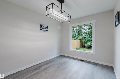 Light gray wood-finish flooring, a contemporary rectangular light fixture, and a large window with white trim - 10423 35 Avenue Nw, Edmonton, AB 