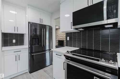White shaker-style cabinetry with black hardware, black stainless steel appliances, modern black tile backsplash, and light wood-finish flooring - 10423 35 Avenue Nw, Edmonton, AB 
