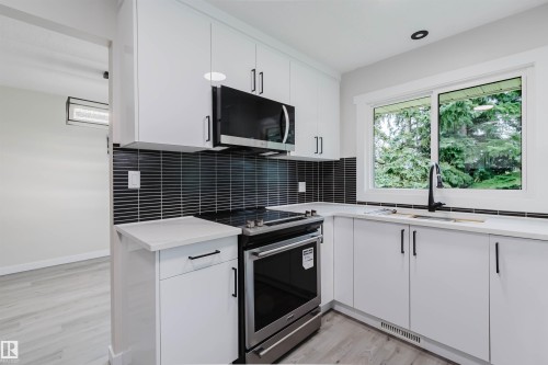 Contemporary kitchen with white cabinetry, stainless steel range and microwave, black tile backsplash, and light-toned countertops - 10423 35 Avenue Nw, Edmonton, AB 