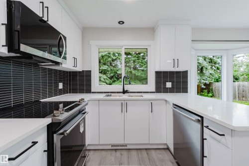 Bright kitchen featuring white cabinetry, stainless steel appliances, a black horizontal tile backsplash, and light countertops - 10423 35 Avenue Nw, Edmonton, AB 