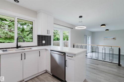 Modern kitchen featuring white cabinetry, a matte black faucet, integrated stainless steel dishwasher, light-toned countertops, and a distinct tiled backsplash - 10423 35 Avenue Nw, Edmonton, AB 