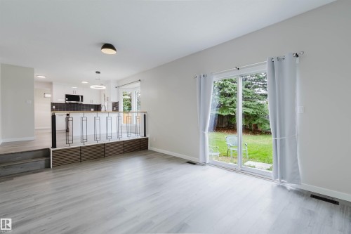 Wood-finish flooring throughout, sliding glass door leading to a grass area, modern open-concept railing, white kitchen cabinetry, and built-in microwave - 10423 35 Avenue Nw, Edmonton, AB 
