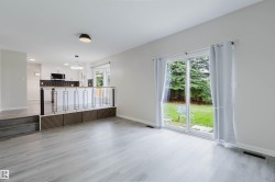 Wood-finish flooring throughout, sliding glass door leading to a grass area, modern open-concept railing, white kitchen cabinetry, and built-in microwave - 