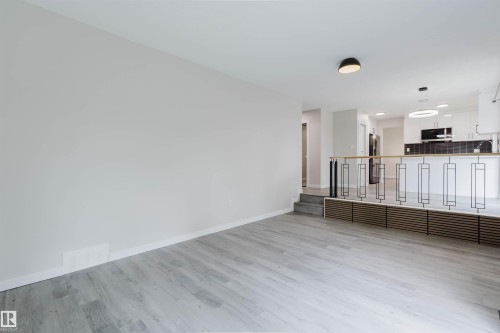 Light wood-finish flooring with a neutral wall color, contemporary railing with black accents, built-in recessed storage, and modern overhead lighting - 10423 35 Avenue Nw, Edmonton, AB 