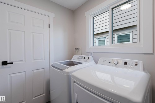 Laundry area featuring a window, white appliances, and a solid panel door with dark hardware - 10423 35 Avenue Nw, Edmonton, AB 
