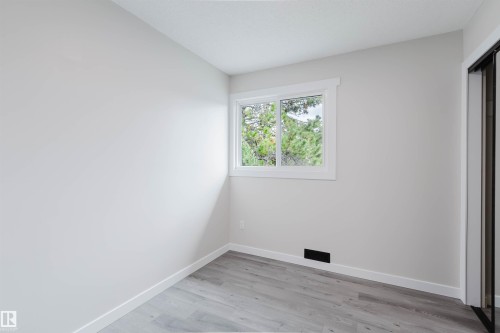 Light gray walls, wood-finish flooring, white window frame, and a closet with a dark frame - 10423 35 Avenue Nw, Edmonton, AB 