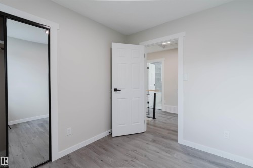 Bright, open bedroom featuring wood-finish flooring, clean white walls, and multiple entry points including a white six-panel door and mirrored closet door - 10423 35 Avenue Nw, Edmonton, AB 