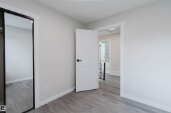 Bright, open bedroom featuring wood-finish flooring, clean white walls, and multiple entry points including a white six-panel door and mirrored closet door - 