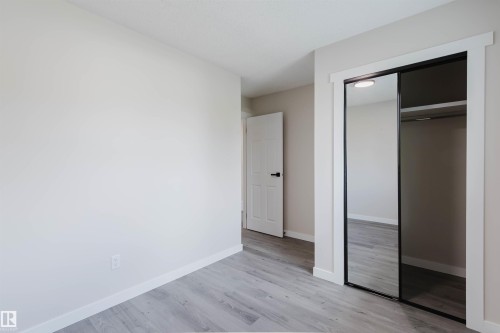 Light-toned wood-finish flooring, white painted walls, white trim, sliding mirrored closet doors, and white interior doors - 10423 35 Avenue Nw, Edmonton, AB 